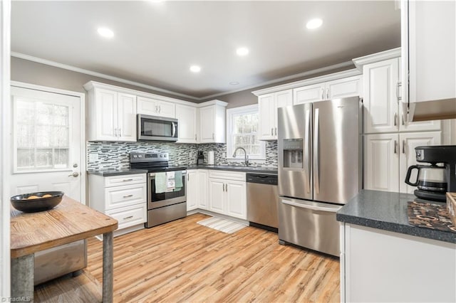 kitchen featuring tasteful backsplash, white cabinetry, ornamental molding, light hardwood / wood-style floors, and stainless steel appliances