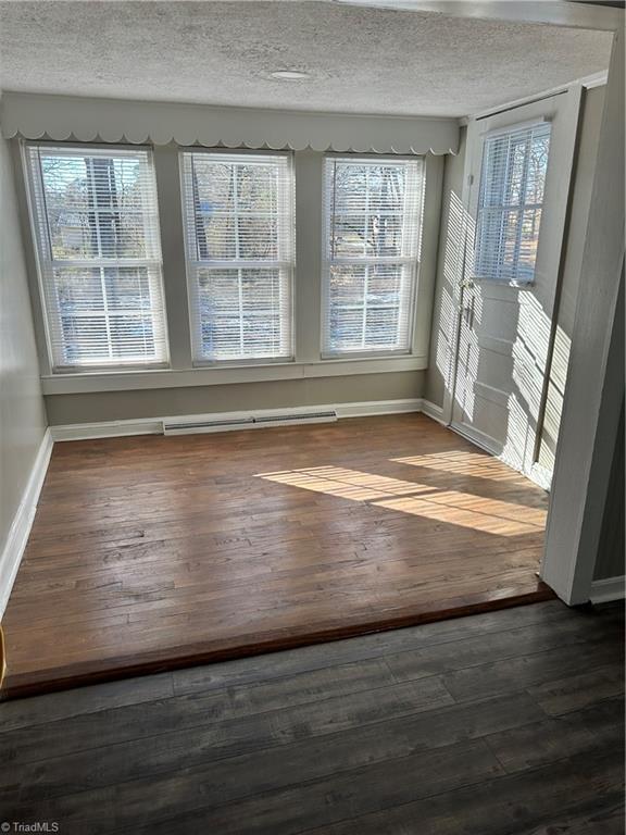 unfurnished dining area with a baseboard radiator, a textured ceiling, and dark hardwood / wood-style flooring