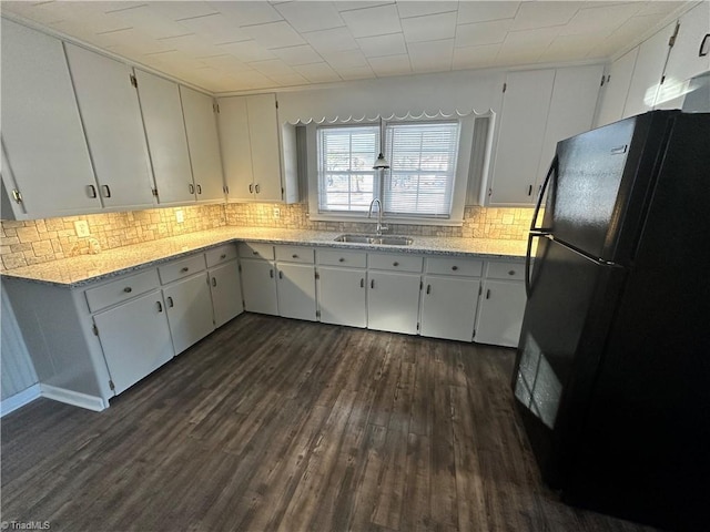 kitchen featuring black refrigerator, white cabinetry, sink, and light stone counters