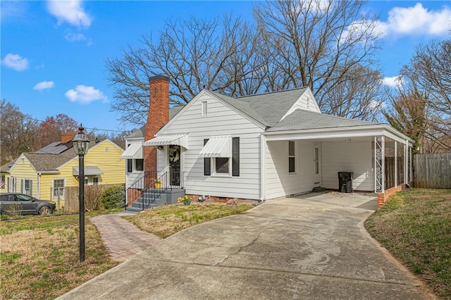 view of front of home with an attached carport, a front yard, fence, roof with shingles, and concrete driveway