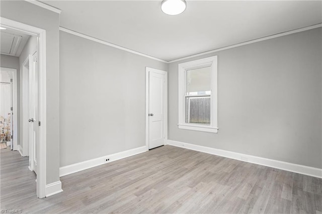 empty room with attic access, wood finished floors, baseboards, and ornamental molding