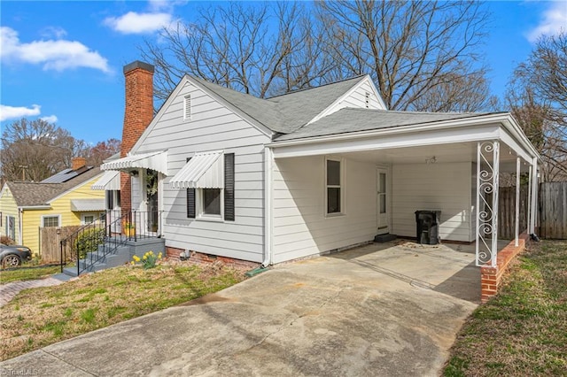 view of side of property featuring concrete driveway, a carport, fence, and roof with shingles