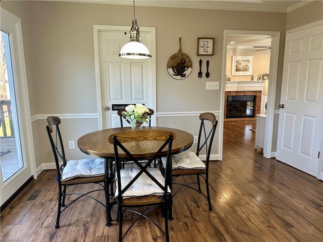 dining space featuring dark hardwood / wood-style flooring, a brick fireplace, and ornamental molding