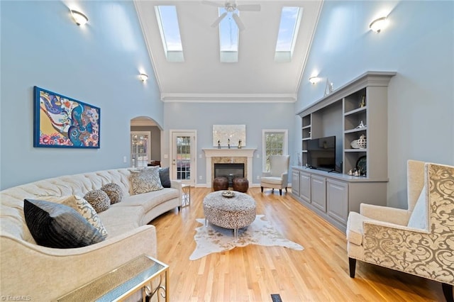 living room featuring light wood finished floors, ceiling fan, arched walkways, a glass covered fireplace, and high vaulted ceiling