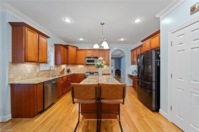 kitchen with a center island, light stone counters, arched walkways, stainless steel appliances, and a sink