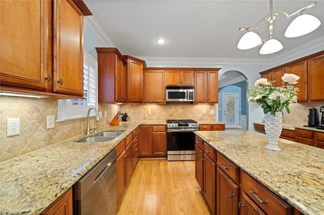 kitchen featuring light stone counters, stainless steel appliances, crown molding, and a sink