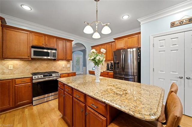 kitchen featuring arched walkways, appliances with stainless steel finishes, light wood-style floors, and ornamental molding