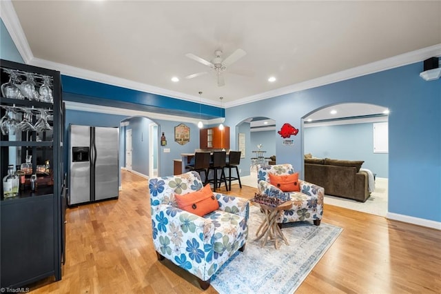 living area with arched walkways, light wood-type flooring, ceiling fan, and ornamental molding