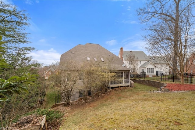 rear view of house featuring a lawn, a chimney, fence, and a sunroom