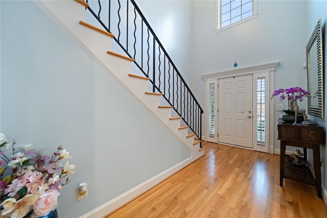 entryway with light wood finished floors, stairs, a high ceiling, and baseboards