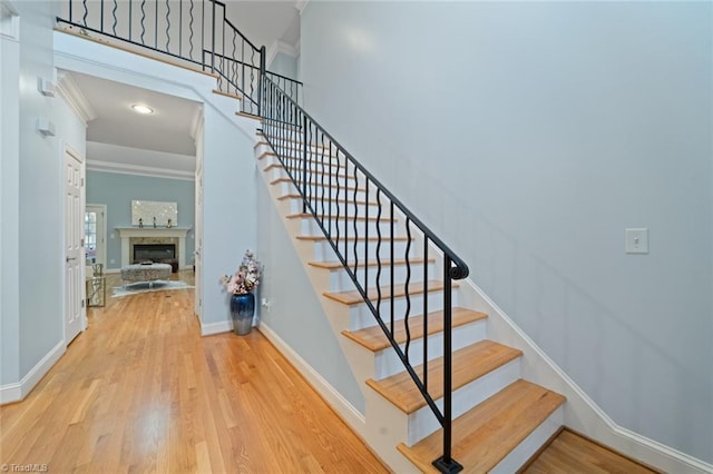 staircase featuring a glass covered fireplace, baseboards, wood finished floors, and ornamental molding