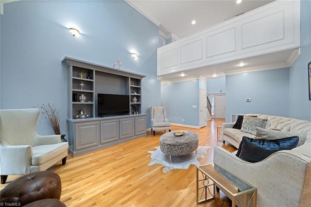 living room featuring light wood-type flooring, baseboards, a towering ceiling, and crown molding