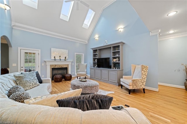 living room with wood finished floors, a fireplace, arched walkways, ceiling fan, and ornamental molding