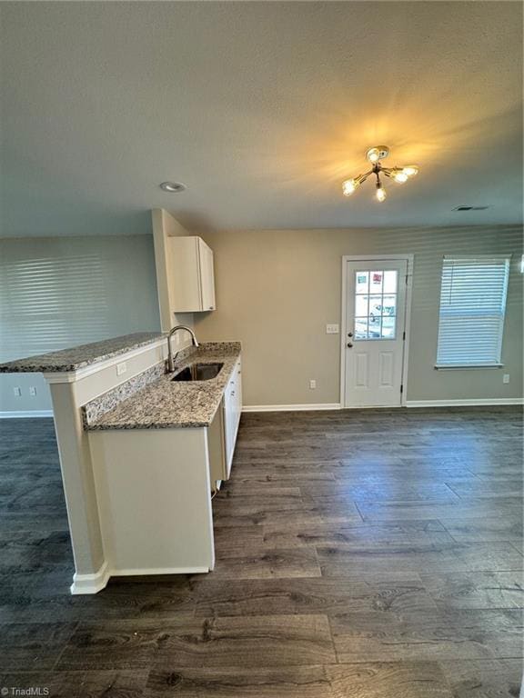 kitchen featuring white cabinetry, kitchen peninsula, light stone countertops, sink, and dark hardwood / wood-style floors