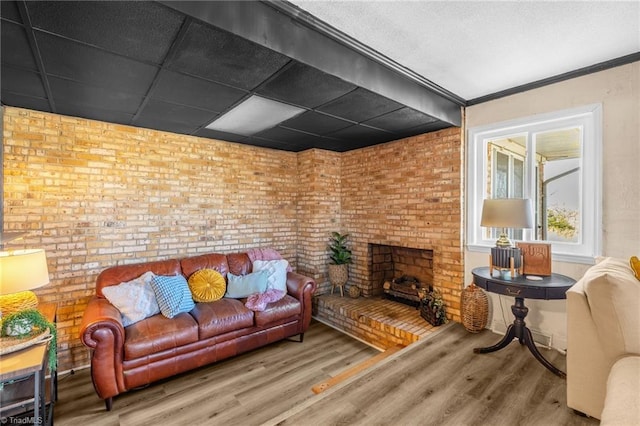 living area with a drop ceiling, a brick fireplace, wood finished floors, and brick wall