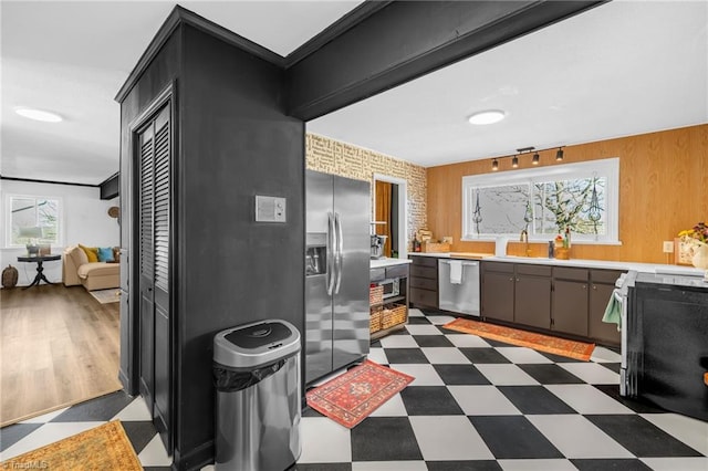 kitchen with wooden walls, dark floors, light countertops, appliances with stainless steel finishes, and a sink