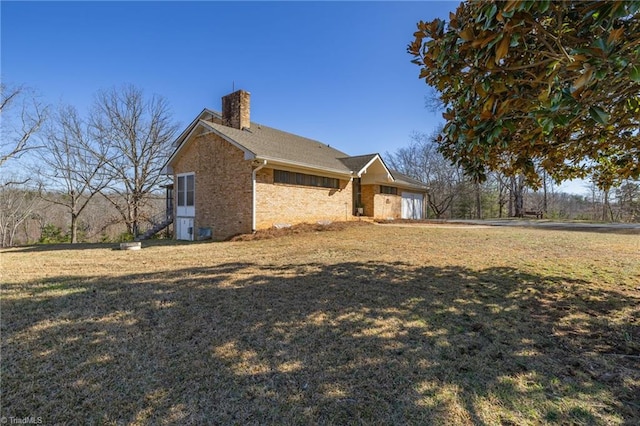 view of side of property featuring brick siding, a yard, an attached garage, and a chimney