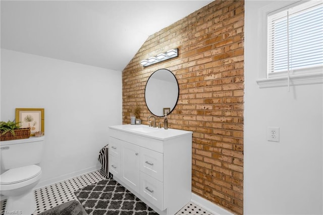 bathroom featuring brick wall, baseboards, toilet, lofted ceiling, and vanity