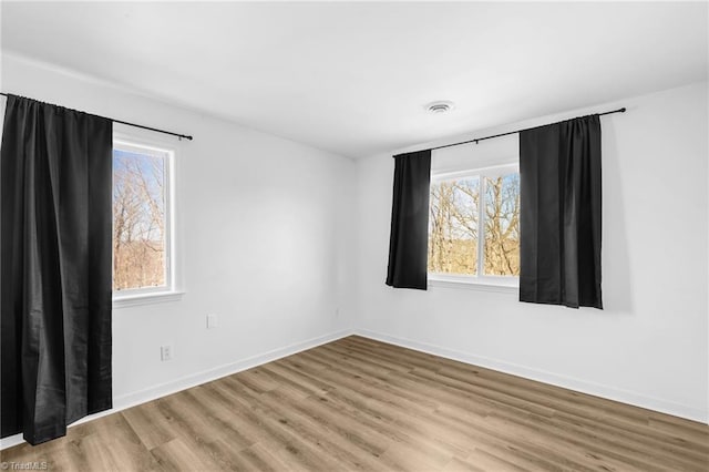 spare room featuring a wealth of natural light, visible vents, baseboards, and light wood-style floors