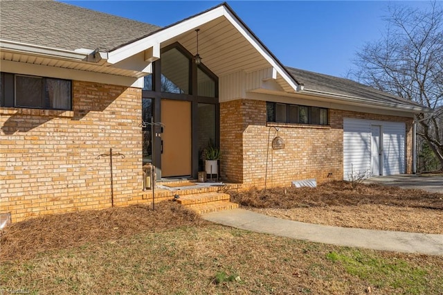 view of exterior entry featuring crawl space, an attached garage, brick siding, and a shingled roof