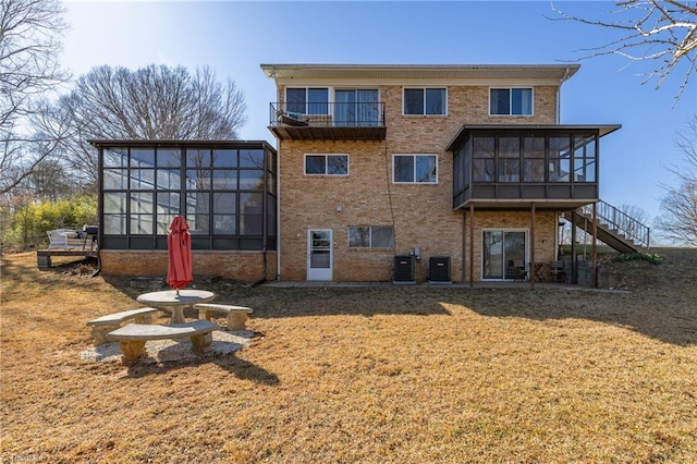 rear view of house featuring a yard, a sunroom, brick siding, central AC unit, and stairs