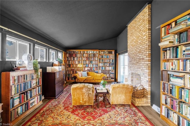 living area featuring vaulted ceiling, wood finished floors, wall of books, and a textured ceiling