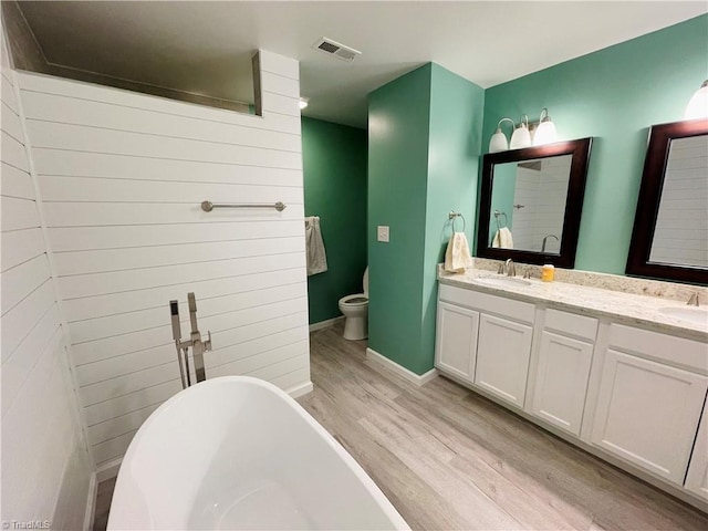 bathroom with toilet, vanity, a bath, and hardwood / wood-style floors