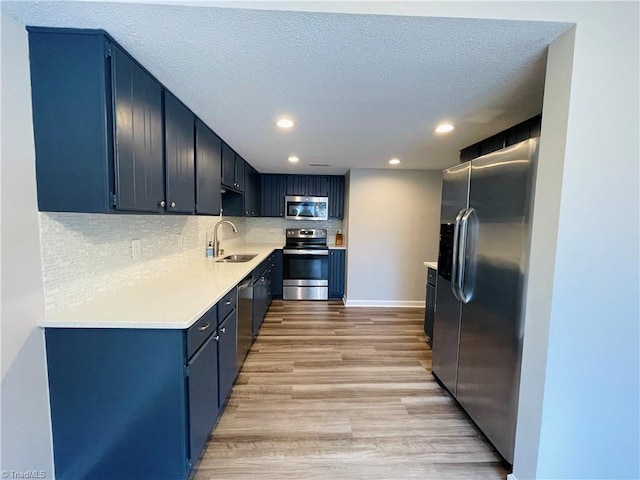 kitchen featuring blue cabinetry, sink, appliances with stainless steel finishes, light hardwood / wood-style floors, and decorative backsplash