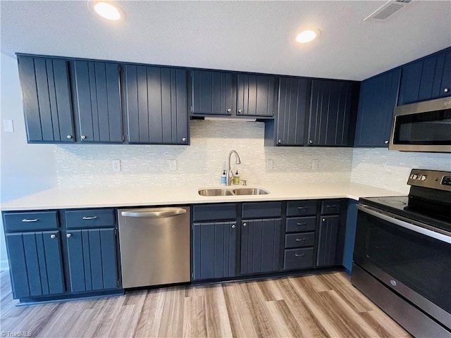 kitchen with blue cabinets, sink, tasteful backsplash, light hardwood / wood-style flooring, and appliances with stainless steel finishes