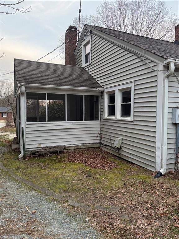 view of property exterior with a shingled roof, a sunroom, and a chimney