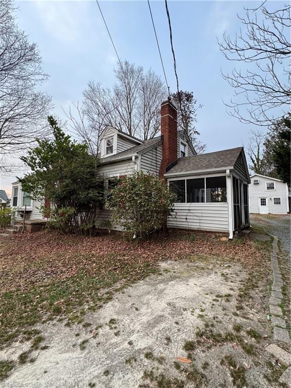 rear view of property with a shingled roof, driveway, a sunroom, and a chimney