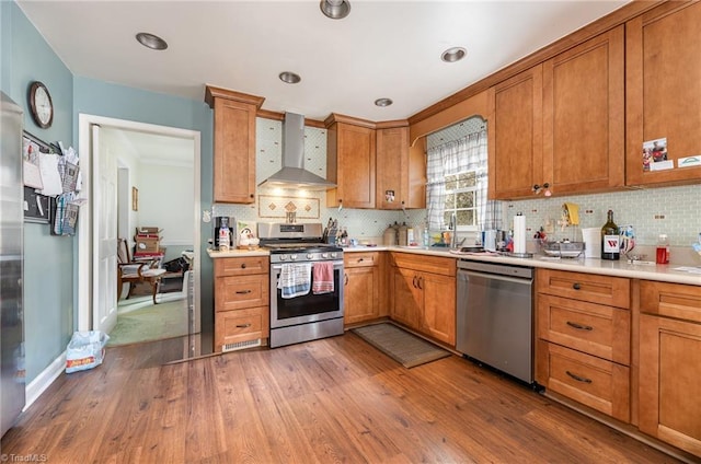 kitchen featuring stainless steel appliances, light countertops, decorative backsplash, wall chimney range hood, and wood finished floors