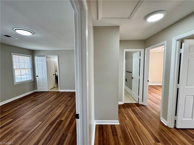 corridor with dark wood-type flooring, baseboards, and visible vents