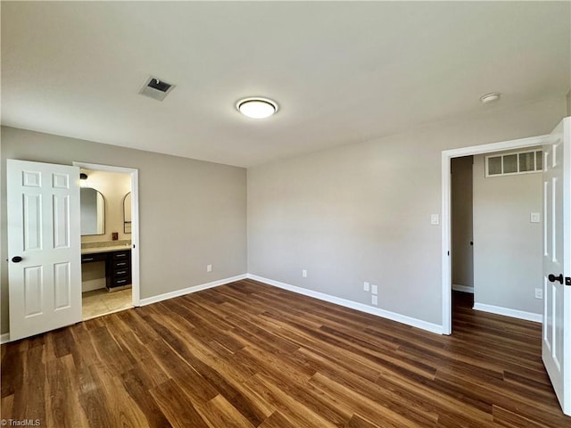 unfurnished bedroom with connected bathroom, visible vents, baseboards, and dark wood-style floors