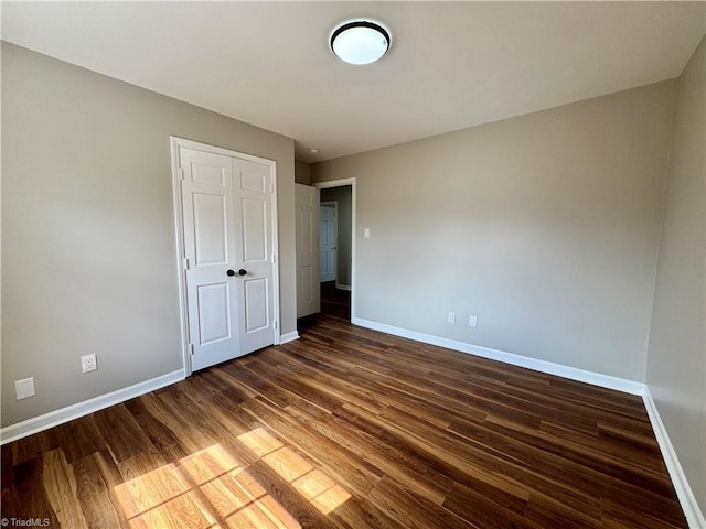 unfurnished bedroom featuring dark wood-type flooring, baseboards, and a closet