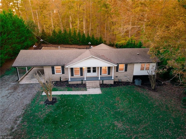 view of front facade featuring covered porch, dirt driveway, an attached carport, a front yard, and a forest view