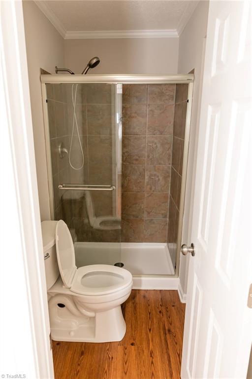 bathroom with a stall shower, wood finished floors, toilet, and ornamental molding