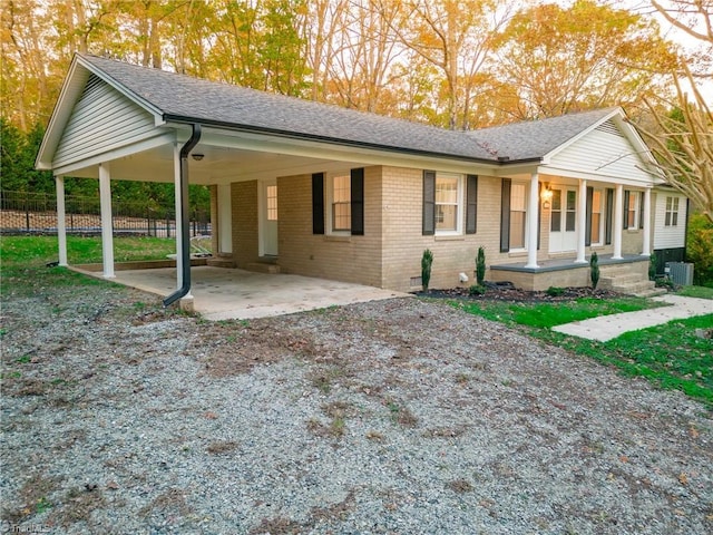 view of front facade featuring a porch, a carport, brick siding, fence, and roof with shingles