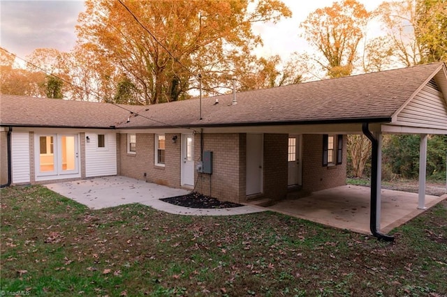 rear view of house with a carport, brick siding, a lawn, and a patio area