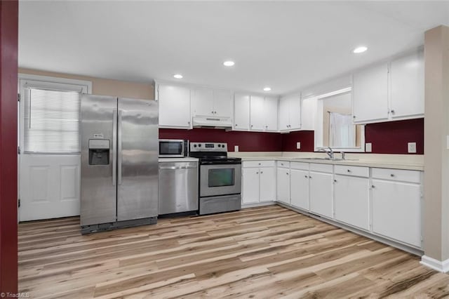 207 Bingham St, Carthage, NC 28327 - kitchen featuring appliances with stainless steel finishes, a sink, under cabinet range hood, light wood-style floors, and white cabinets