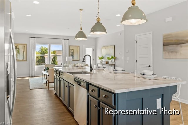 kitchen featuring appliances with stainless steel finishes, hanging light fixtures, a center island with sink, and light stone countertops