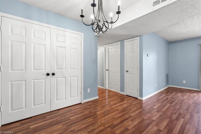 interior space featuring a notable chandelier, multiple closets, a textured ceiling, and dark hardwood / wood-style flooring