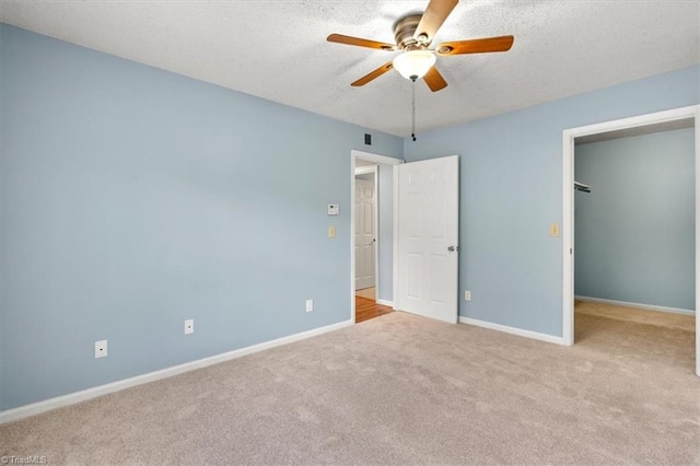 unfurnished bedroom with light carpet, ceiling fan, a walk in closet, and a closet