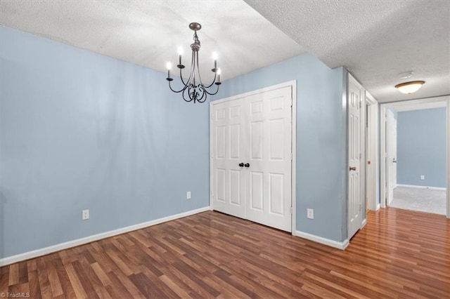 spare room featuring a textured ceiling, wood-type flooring, and a notable chandelier