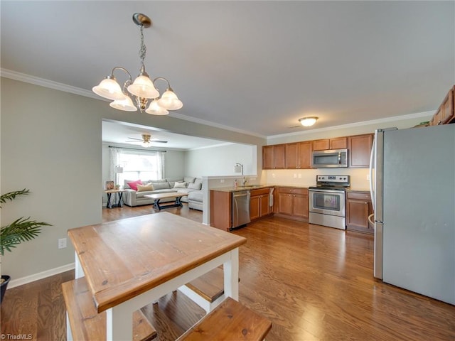 kitchen featuring dark wood-type flooring, appliances with stainless steel finishes, decorative light fixtures, and crown molding