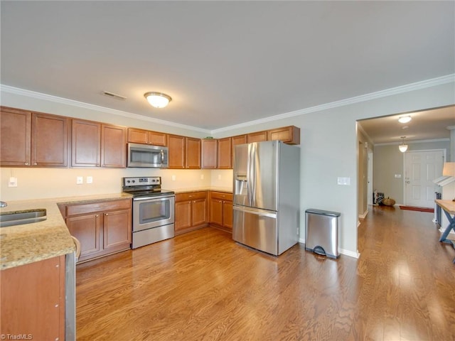 kitchen featuring stainless steel appliances, light hardwood / wood-style floors, sink, ornamental molding, and light stone countertops