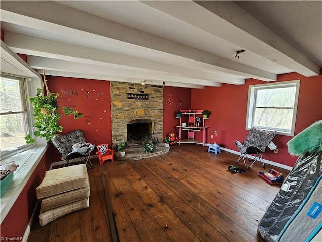 living area with wood-type flooring, baseboards, a stone fireplace, and beam ceiling