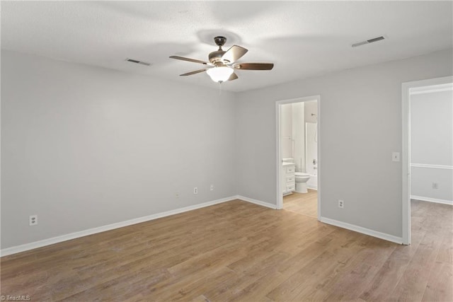 unfurnished bedroom featuring ceiling fan, ensuite bathroom, a walk in closet, and light wood-type flooring