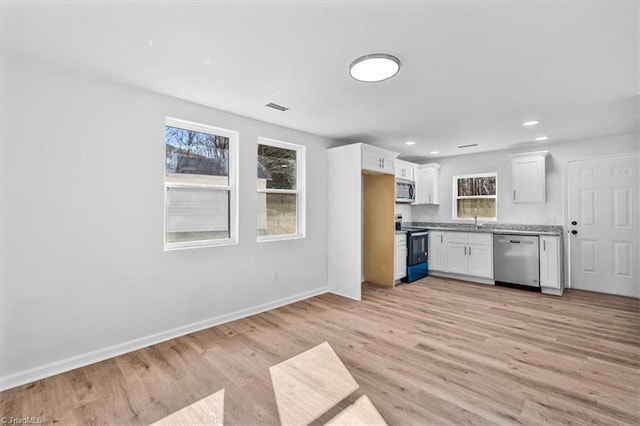 kitchen featuring appliances with stainless steel finishes, sink, white cabinets, light stone counters, and light hardwood / wood-style flooring