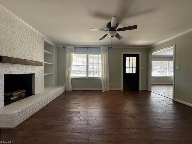 unfurnished living room featuring baseboards, built in features, dark wood-type flooring, crown molding, and a brick fireplace